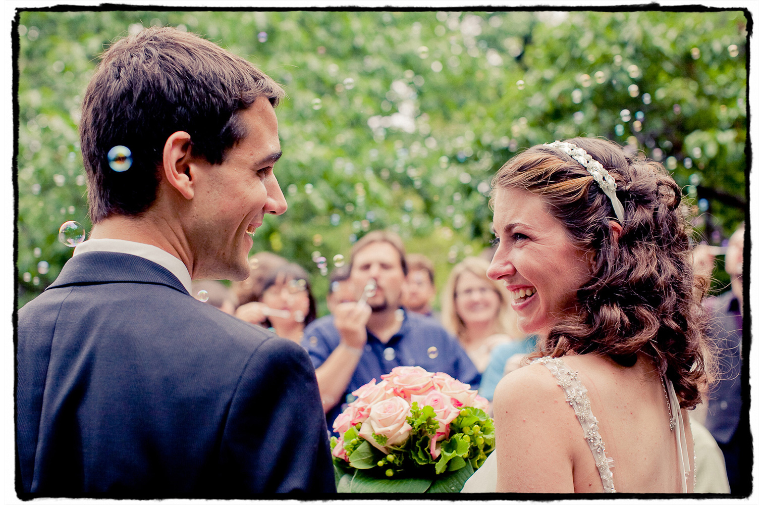 Julie and Andy smile lovingly at one another as guests blow bubbles in celebration of the conclusion of their ceremony at The Shakespeare Garden in Central Park.