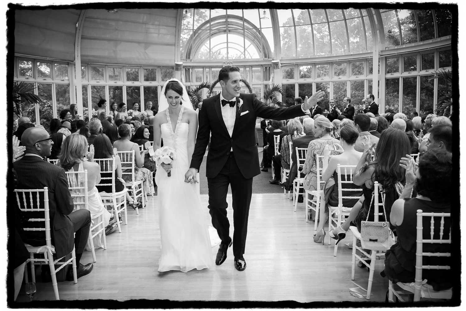 Jessica and Stephen wave to their guests as they walk back down the aisle in The Palm House at Brooklyn Botanic Garden.